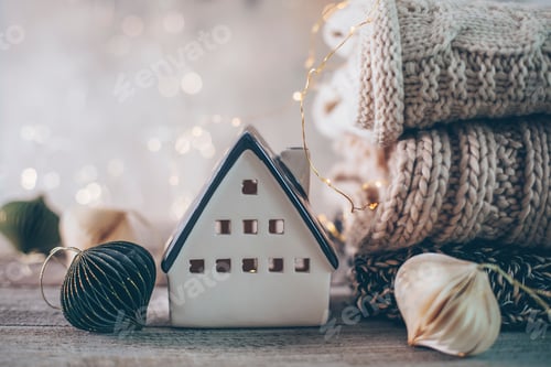 Preview: Stack of cozy winter knitted sweaters, ceramic house on a blurred background with bokeh