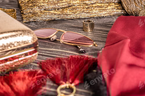 Preview: close up view of fashionable feminine earrings, sunglasses and purse arranged on wooden tabletop