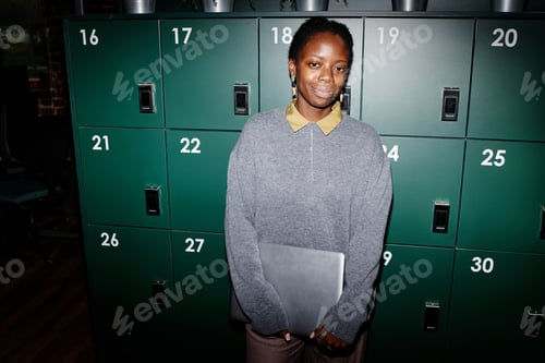 Preview: Portrait of Young Adult Black Woman Standing Holding Laptop in Modern Office