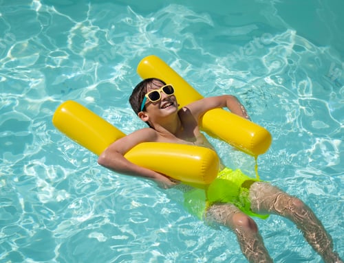Preview: Boy relaxing on inflatable mattress in swimming pool wearing sunglasses