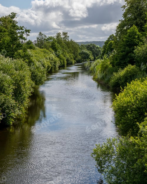 Preview: A river with lush green trees on both sides. Sky with clouds reflects in water.