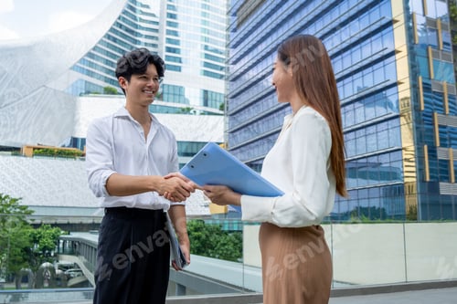 Preview: Asian businessman and businesswoman making handshake outdoors in city.