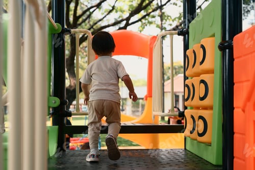 Preview: Back view of toddler enjoying playtime at a colorful outdoor playground