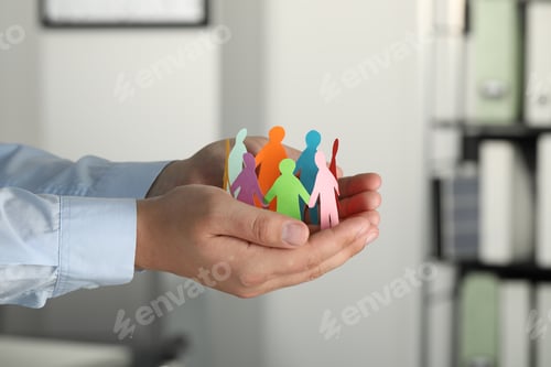 Preview: Man holding paper human figures in office, closeup. Diversity and Inclusion concept