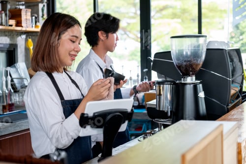 Preview: Asian barista or coffee maker woman clean cup of coffee while co-worker set machine