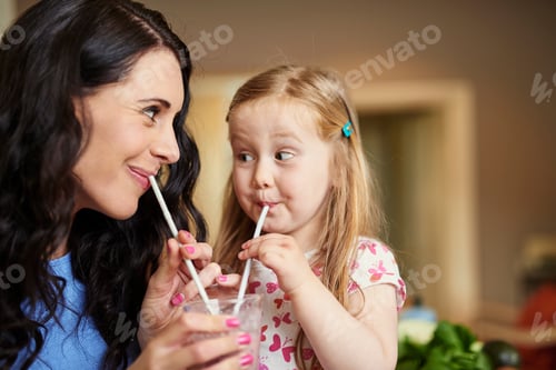 Preview: Mother and daughter face to face drinking smoothie with straws