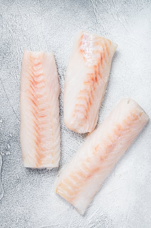 Preview: Raw Norwegian cod fish fillet on kitchen table. White background. Top view