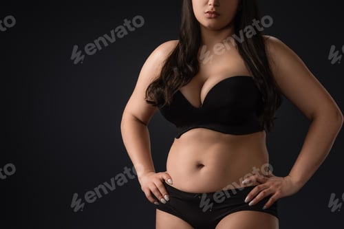 Preview: Cropped view of young size plus woman in underwear on black background