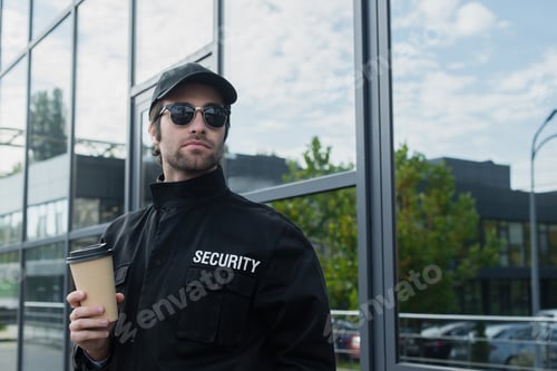 Preview: guard in black uniform and sunglasses holding coffee to go outdoors