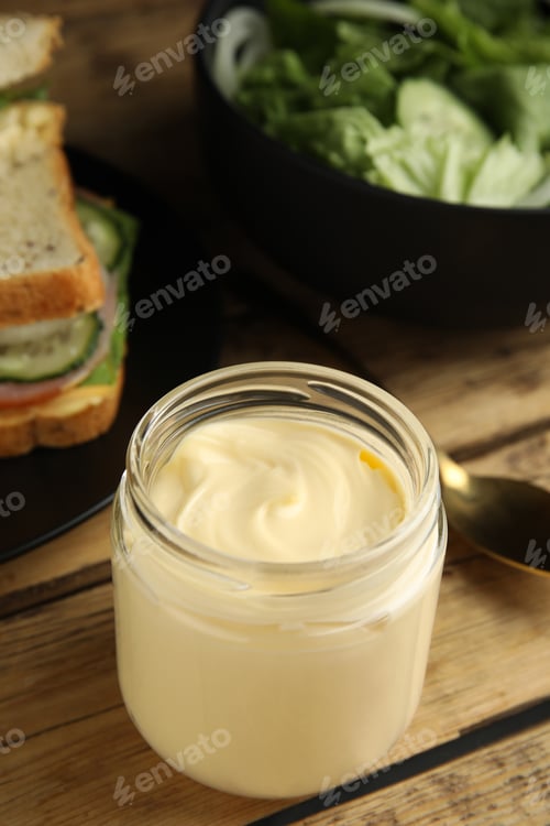 Preview: Jar of delicious mayonnaise near fresh sandwiches on wooden table