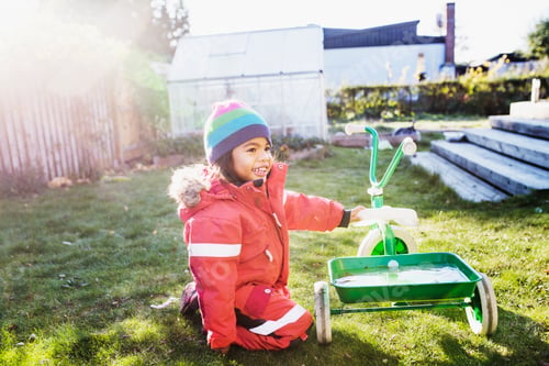 Preview: Girl (4-5) with tricycle in garden