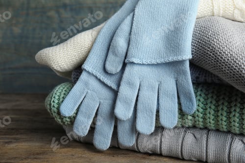 Preview: Stacked sweaters and gloves on wooden table, closeup. Autumn clothes