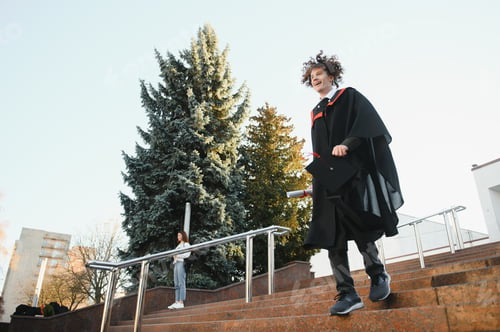 Preview: Low angle portrait of happy triumphant male graduate standing near university