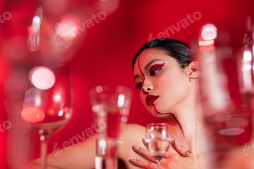 Preview: low angle view of nude asian woman with bright creative visage touching bare shoulder near blurred