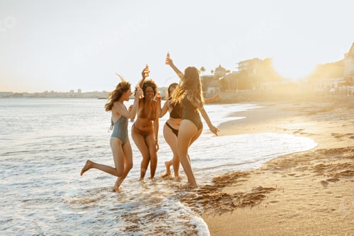 Preview: Joyful young multiracial ladies in swimsuits dancing, holding beer bottles, enjoying summer beach