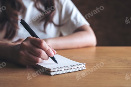 Preview: Closeup image of a woman writing down on a white blank notebook on table