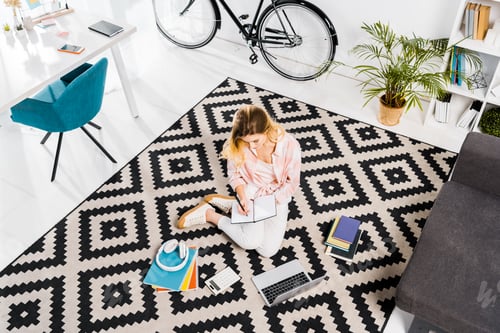 Preview: Woman sitting on carpet and writing in notebook at home