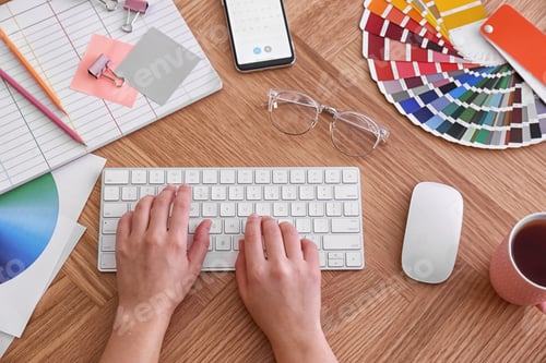 Preview: Designer working on computer at wooden table, top view