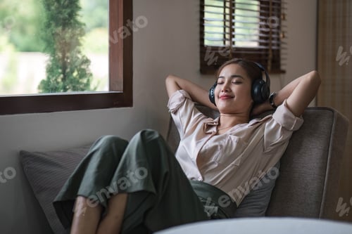 Preview: Happy woman relaxing in her sofa at home, Smiling girl is listening to music with headphones and