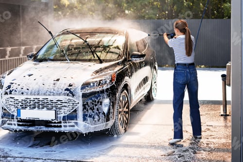 Preview: Woman washing her car with high pressure washer at self service car wash