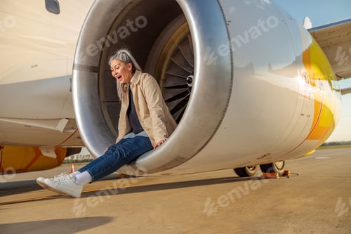 Preview: Joyful woman sitting in airplane engine at airport