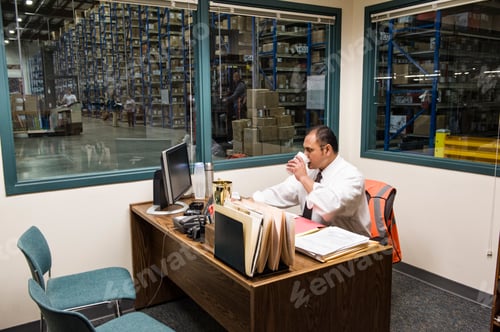 Preview: Hispanic American executive working on a computer in an office in the middle of a large distribution