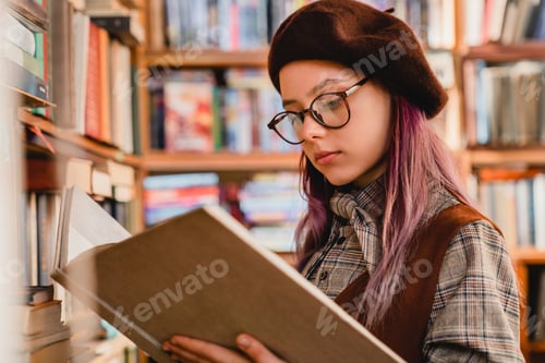 Preview: Intelligent young caucasian girl in glasses reading a book at the library