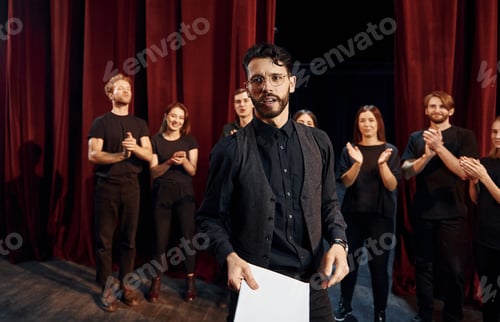 Preview: Man is practicing his role. Group of actors in dark colored clothes on rehearsal in the theater