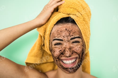 Preview: Young smiling woman applying coffee scrub mask on face