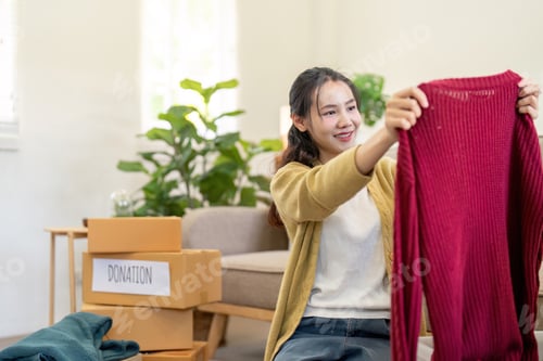 Preview: Excited woman showcasing a red sweater for donation, encouraging a culture of giving