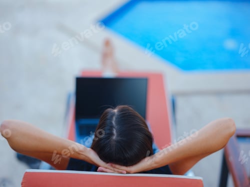Preview: Young business woman working at computer by hotel pool.