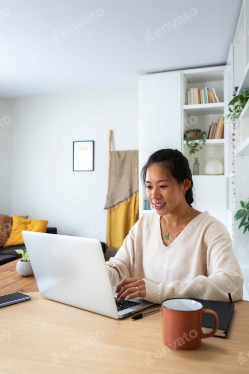 Preview: Asian female working using laptop. Smiling Chinese woman working with computer at home. Vertical