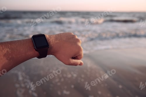 Preview: Man checking smart watch on beach at sunset, closeup