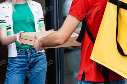 Preview: Cropped view of courier giving pizza boxes to woman near building on urban street