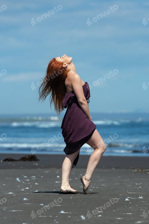 Preview: Woman in long dress standing on sandy beach with head looking upward and eyes closed, sunbathing