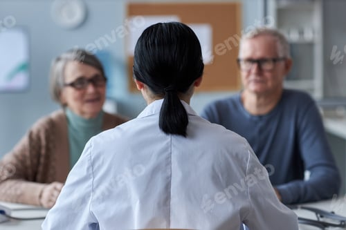 Preview: Back of female doctor working with senior couple in medical clinic
