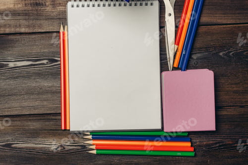 Preview: notepads colored pencils pens scissors on wooden background top view