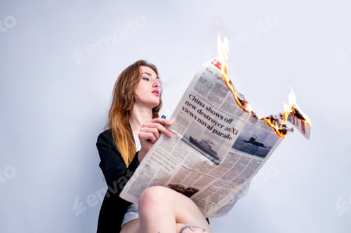 Preview: A stylish blonde businesswoman smoking and holding a lit fire newspaper in studio.