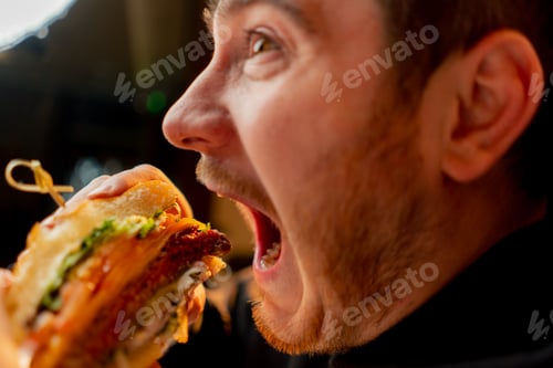 Preview: close-up man with enjoy biting delicious juicy cheeseburger in cafe restaurant junk food calories