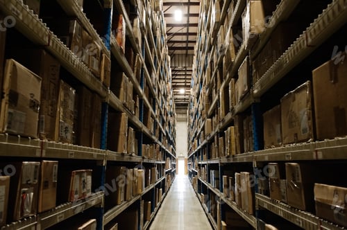 Preview: View down an aisle of racks holding cardboard boxes of product on pallets in a large distribution