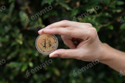 Preview: Young man holding BTC Bitcoin in hand with green bush in background