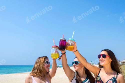 Preview: group of happy young women or female friends toasting non alcoholic drinks on summer beach