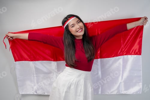 Preview: Excited young Asian woman is spreading Indonesian flag at her back and smiling.