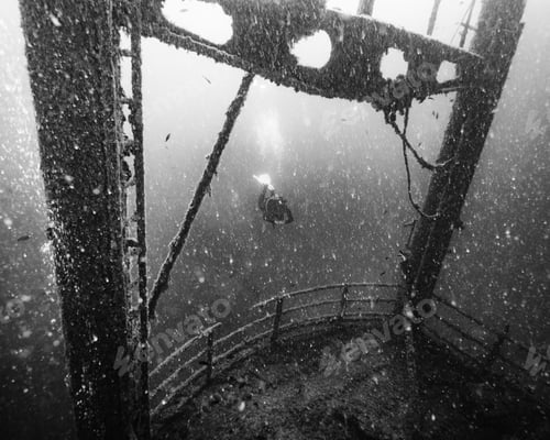 Preview: High angle shot of a person diving near an old wrecked ship shot in grayscale