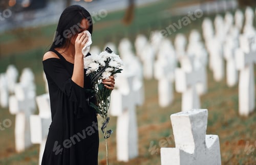 Preview: Young woman in black clothes visiting cemetery with many white crosses