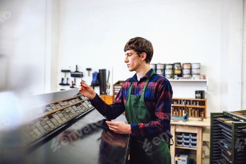 Preview: Profile shot of young craftsman looking at metal letterpress spacing in a book arts workshop