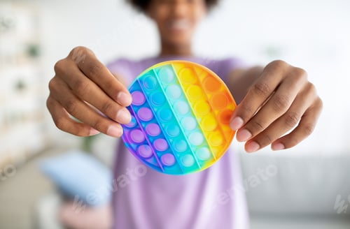 Preview: Cropped view of black teenager holding POP IT toy in outstretched hands at home, closeup