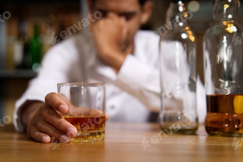Preview: Drunk man sitting at the bar in pub and holding whisky glass in right hand.