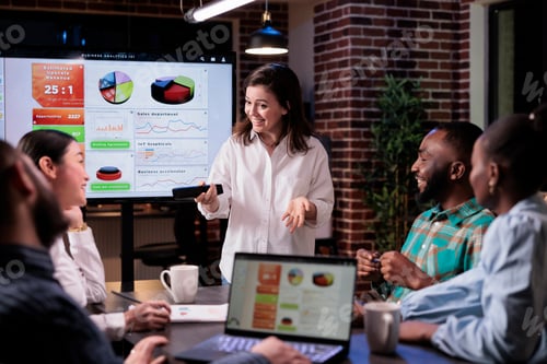 Preview: Smiling caucasian woman in late night meeting presenting business analytics to happy team