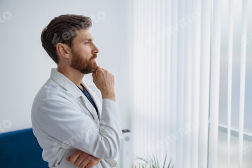 Preview: Portrait of handsome doctor in uniform standing in medicine clinic hall and looking away